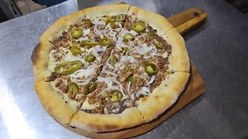 Pizza de carne molida con jalapeño y cebolla, sobre pala de madera